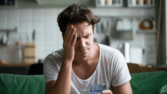 man with a headache clutching his head and holding a glass of water